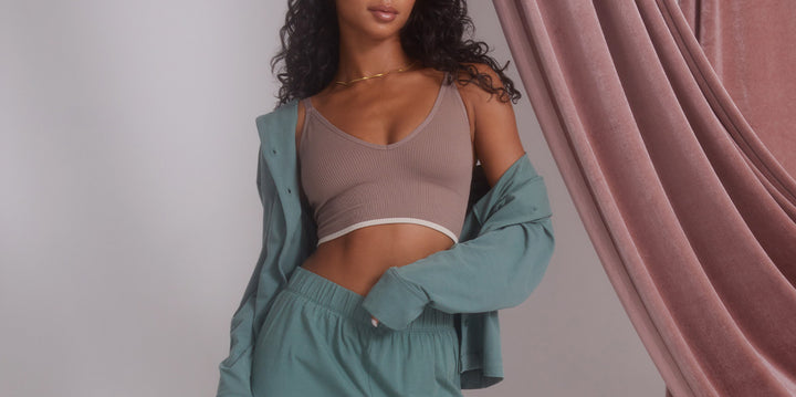 Model Ally wearing the Perfect Pima Long Sleeve Shirt and Pants in Rainforest, layered over a the Lounge Rib Triangle Bralette. She poses confidently against a soft pink curtain backdrop, showcasing the relaxed and comfortable fit of the loungewear set.